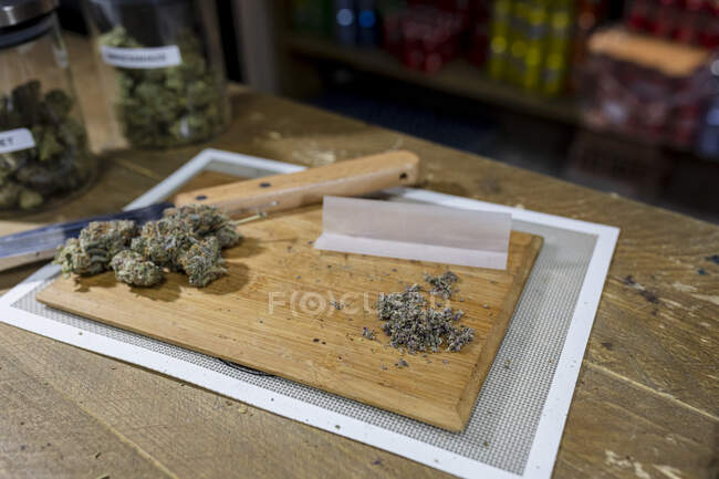 Cigarro de papel na faca contra botões florais de cânhamo seco na tábua de corte no quarto — Fotografia de Stock