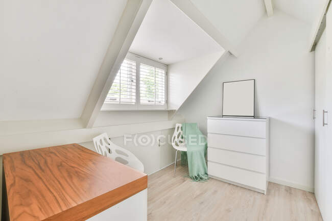 Интерьер небольшой светлой мансардной комнаты с белым шкафом и шкафами в квартире в дневное время — стоковое фото