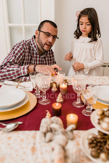 Dad sitting near daughter and lightning candles placed on festive table served for Xmas celebration — Stock Photo