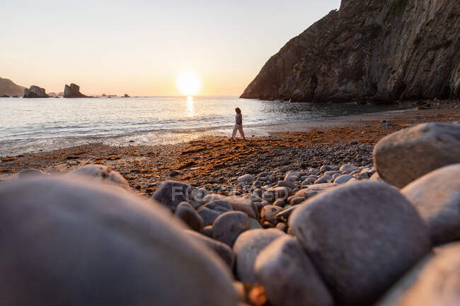 Femmina passeggiando sulla riva grezza contro le montagne e l'oceano ondulato al tramonto nelle Asturie Spagna — Foto stock