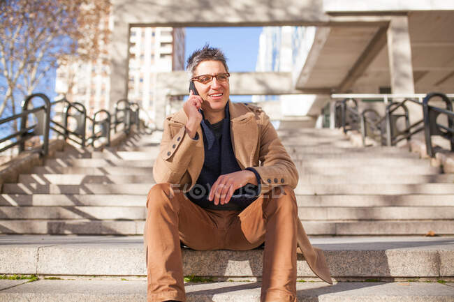 Stilvoller junger Mann in Brille und lässiger Kleidung sitzt auf der Treppe — Stockfoto