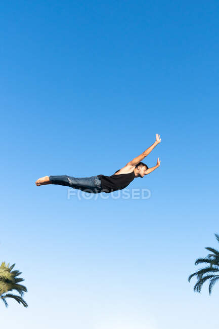 Знизу з боку енергійного спортсмена в модному одязі, що виконує трюк проти блакитного неба на сонячному світлі — стокове фото