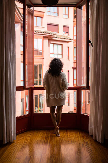 Rückenansicht Ganzkörper der barfüßigen anonymen Frau mit lockigem Haar, die in der Nähe des geöffneten Fensters in der Wohnung steht — Stockfoto