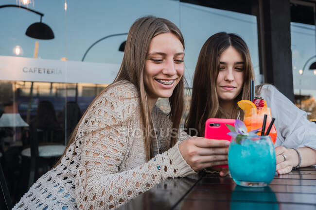 Migliori amiche con bicchieri di bevande rinfrescanti che navigano sul cellulare a tavola nel caffè urbano — Foto stock