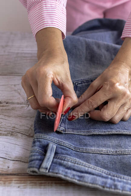 From above anonymous female dressmaker using chalk to draw line near pocket of jeans on wooden table in workshop — Stock Photo