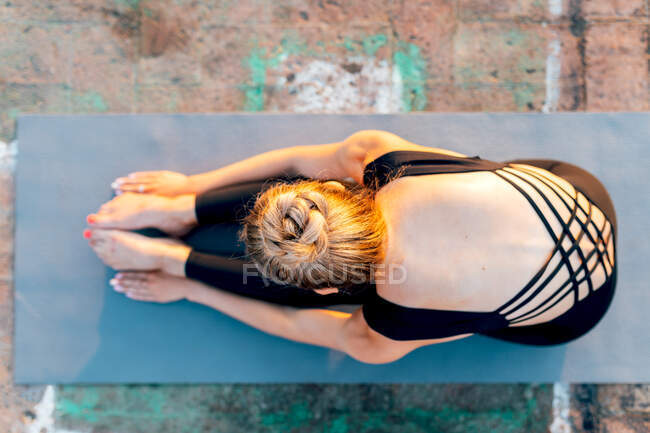Полное тело сверху гибкой женщины практикующей Пасхимоттанасану на спортивном коврике на крыше на закате — стоковое фото