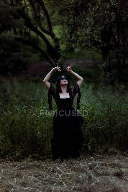 Mystic witch with painted face dancing with arms in gloomy woods and looking up — Stock Photo