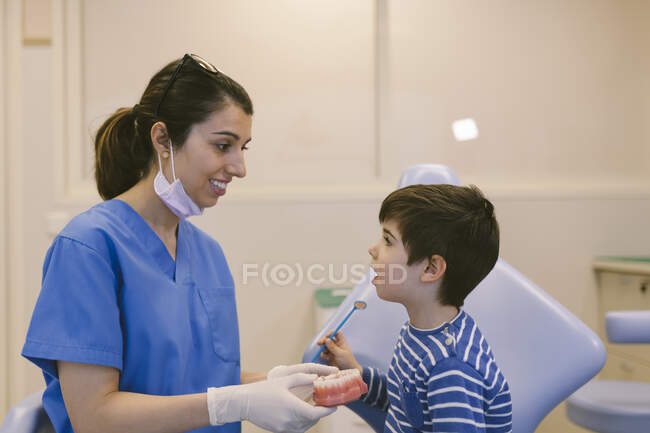 Ortodontista feminina ensinando paciente com escova de dentes para escovar os dentes no modelo de mandíbula na clínica odontológica — Fotografia de Stock