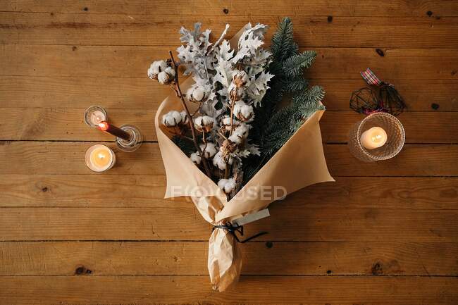 From above of festive Christmas bouquet with branches of cotton and fir placed on wooden table with candles in room — Stock Photo