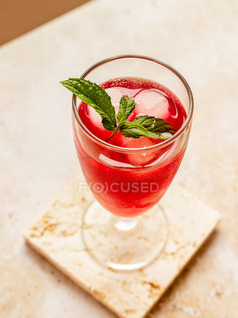 From above of tasty refreshing red beverage with ice cubes and aromatic mint leaves in glass on coaster — Stock Photo