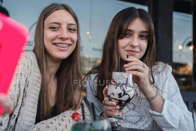 Meilleures amies avec des verres de boissons rafraîchissantes prenant autoportrait sur téléphone portable à la table dans un café urbain — Photo de stock