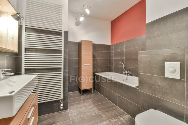 Interieur des Master-Badezimmers mit Badewanne in der Nähe von Schrank und Waschbecken über Schrank unter Lampen an der Decke — Stockfoto