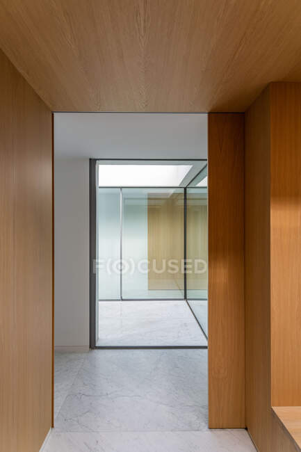 Minimalist interior of spacious corridor with wooden and glass walls and marble tiled floor in sunlight — Stock Photo
