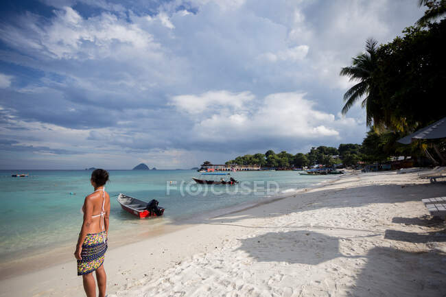 Rückansicht einer Touristin, die das azurblaue Meer am Sandstrand mit Booten und tropischen Bäumen in Malaysia bewundert — Stockfoto