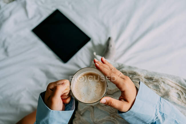 Зверху урожай жінка в сорочці з чашкою ароматичної кави і таблетки вдома — стокове фото