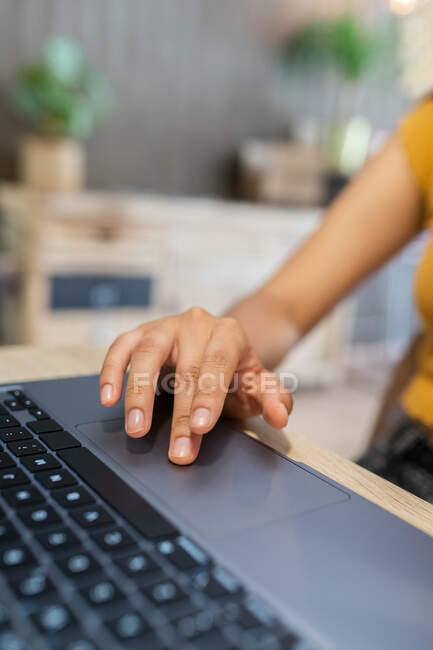 Cultivado joven emprendedora irreconocible sentado a la mesa y navegar netbook mientras se trabaja en el lugar de trabajo moderno - foto de stock