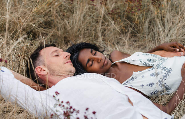 Unshaven man with Indian female partner sleeping on meadow in daytime — Stock Photo