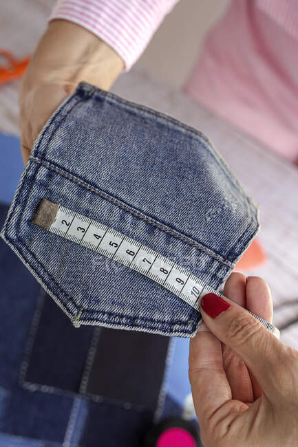 Hohe Schnittwinkel anonyme Schneiderin misst Jeanstasche auf Holztisch am Tag — Stockfoto