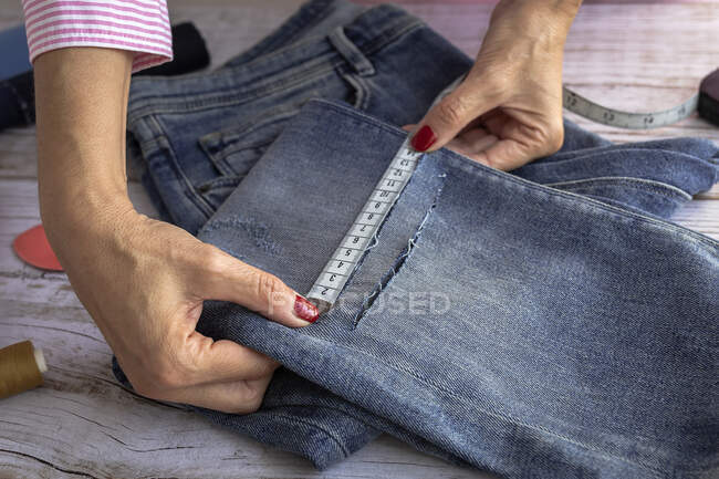 From above of crop anonymous female dressmaker using measuring tape while sewing jeans in atelier in daytime — Stock Photo