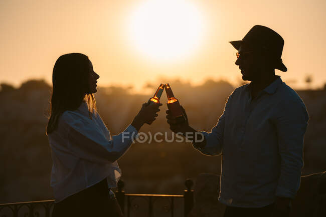 Seitenansicht eines Paares mit Bier, das sich beim Sonnenuntergang auf dem Balkon in Kappadokien, Türkei, anschaut — Stockfoto