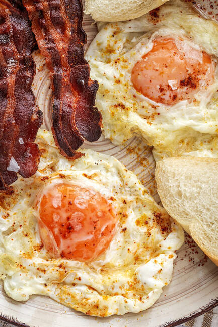 Sabrosos huevos soleados con tiras de tocino frito en el plato - foto de stock