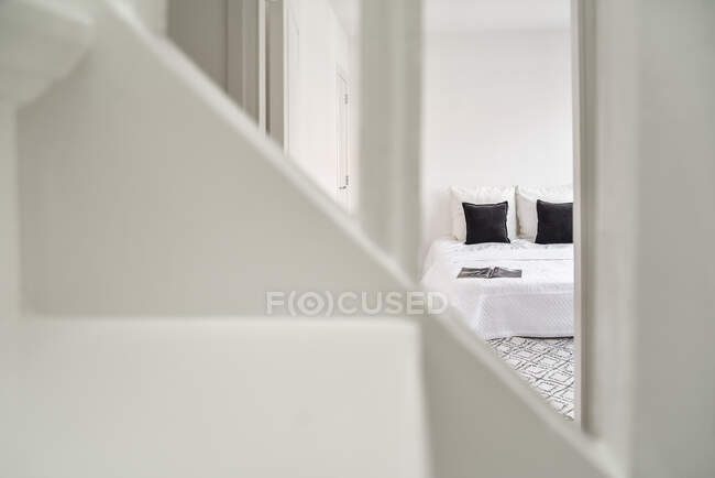 View through handrail of staircase on doorway to bedroom with white bed and black cushions in house — Stock Photo