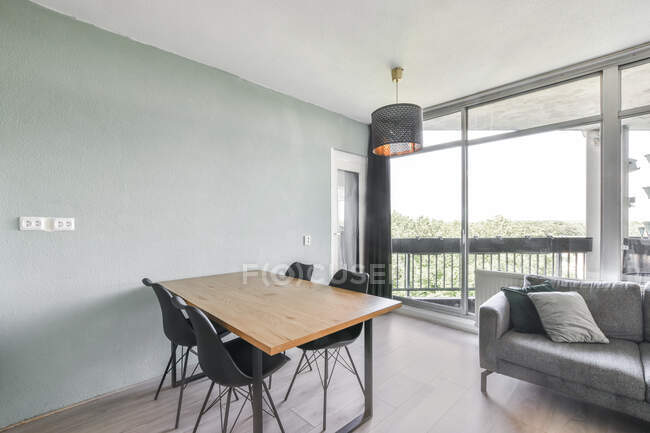 Interno di moderno spazioso appartamento con divano ad angolo vicino tavolo e sedie in legno sotto la lampada — Foto stock