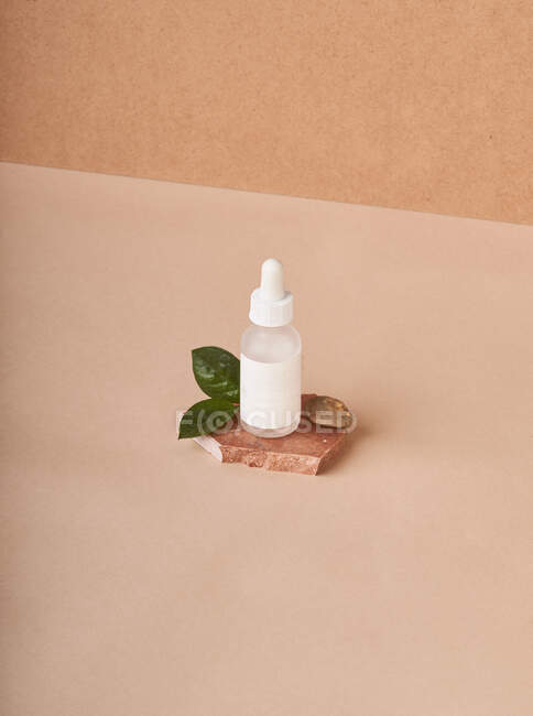 Pequena garrafa branca de soro cosmético colocada em peças de pedra de mármore marrom empilhadas em tecido no fundo bege — Fotografia de Stock