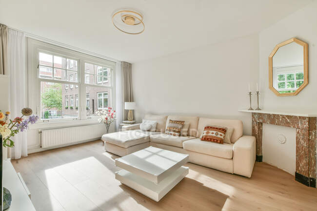 Интерьер просторной гостиной с удобным диваном с подушками и стильными элементами в современной квартире в солнечный день — стоковое фото