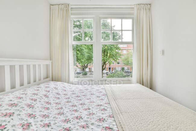 Intérieur minimaliste de la chambre à coucher avec lit confortable contre la fenêtre et les murs de lumière en journée — Photo de stock