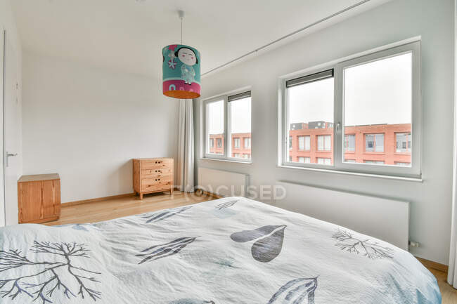 Edredón con adorno de ramita en la cama contra inodoro y ventanas en el apartamento con ilustración en la lámpara - foto de stock