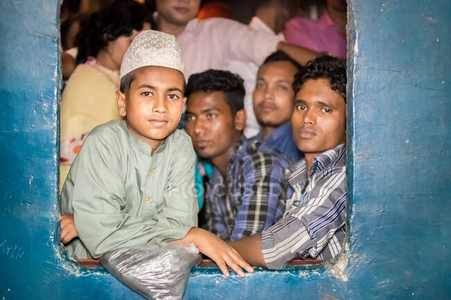 INDIEN, BANGLADESCHEN - 2. DEZEMBER 2015: Ethnischer Junge auf überfüllten Zugfenstern, Männer in Freizeitkleidung blicken in die Kamera — Stockfoto