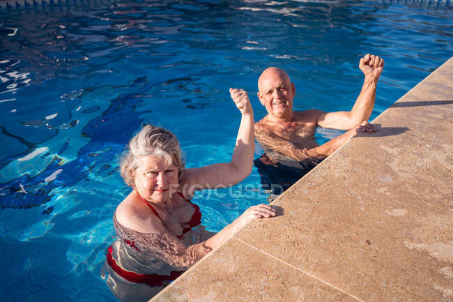 Alto ângulo de casal sênior em trajes de banho com punhos levantados nadando na piscina azul limpa — Fotografia de Stock