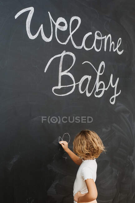 Side view of unrecognizable child with chalk looking away against blackboard with drawn hearts and letters — Stock Photo