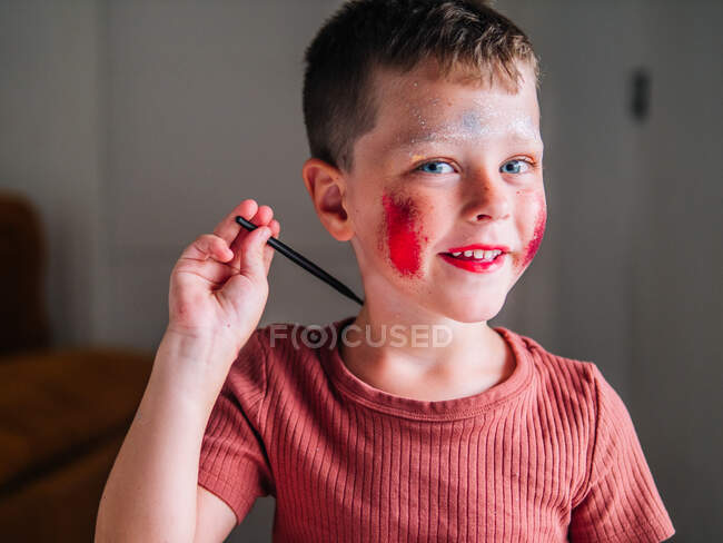 Чарівна дитина з аплікатором для макіяжу, дивлячись на камеру за столом з вітряною палітрою — стокове фото