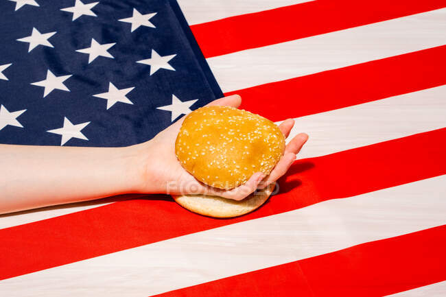 Ernte unkenntliche Person mit Sesam-Brötchen-Hälften auf USA-Flagge mit Sternen- und Streifenornament am Unabhängigkeitstag — Stockfoto