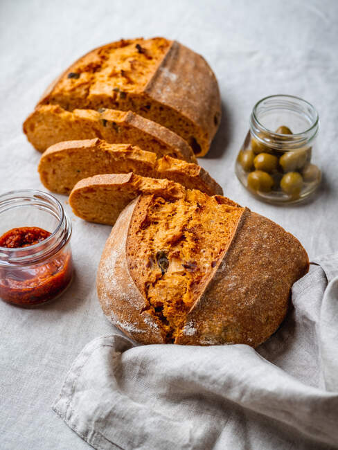 Dall'alto pane di pane di taglio messo su tavolo vicino a salsa di pesto rossa e vaso di olive verdi — Foto stock
