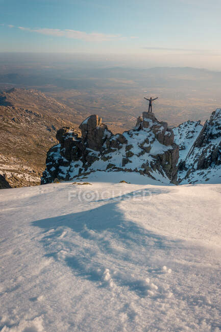 Vista posteriore del viaggiatore irriconoscibile in piedi con le braccia alzate sulla cima rocciosa della Sierra de Guadarrama in inverno alla luce del giorno — Foto stock