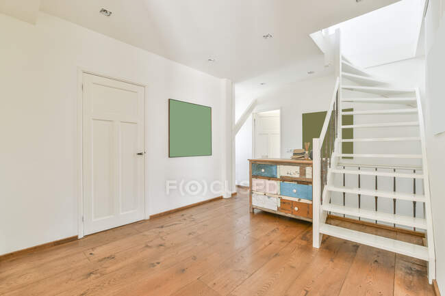 Scala bianca ondulata sopra parquet con tavolo invecchiato contro pannello e porta in corridoio a casa — Foto stock