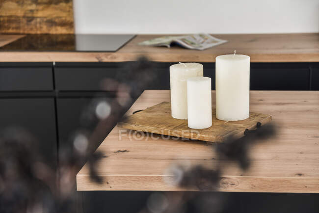 Velas blancas colocadas sobre una mesa de madera contra una encimera - foto de stock