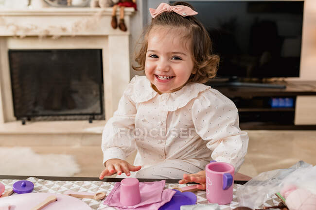 Содержание малыша ребенок с луком на волосах играть с пластиковыми игрушками, глядя на камеру в гостиной — стоковое фото