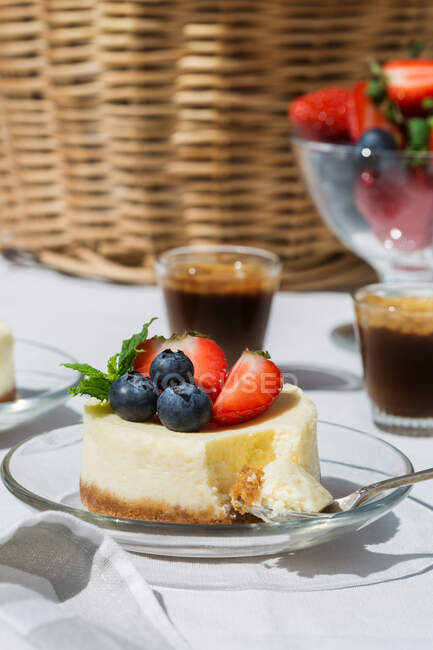 Bolo de queijo doce saboroso com mirtilos e morangos servido em mesa de vidro perto de xícaras de café — Fotografia de Stock
