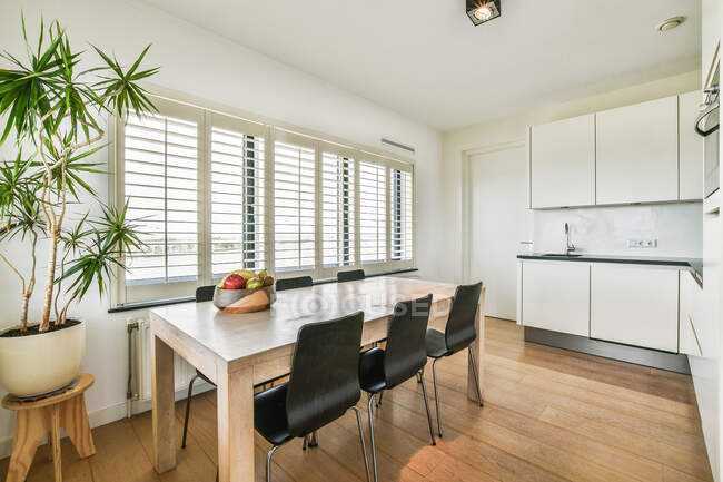 Sala de jantar contemporânea e cozinha interior com mesa contra construído em forno e capuz acima fogão em casa de luz — Fotografia de Stock