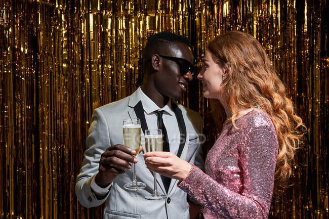 Ritaglia sincera giovane donna abbracciando elegante fidanzato nero mentre tintinnare bicchieri di champagne durante la celebrazione di Capodanno — Foto stock