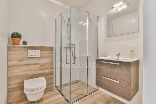 Скляна душова кабіна між туалетом і раковиною під дзеркалом, що звисає на плитці у ванній — стокове фото