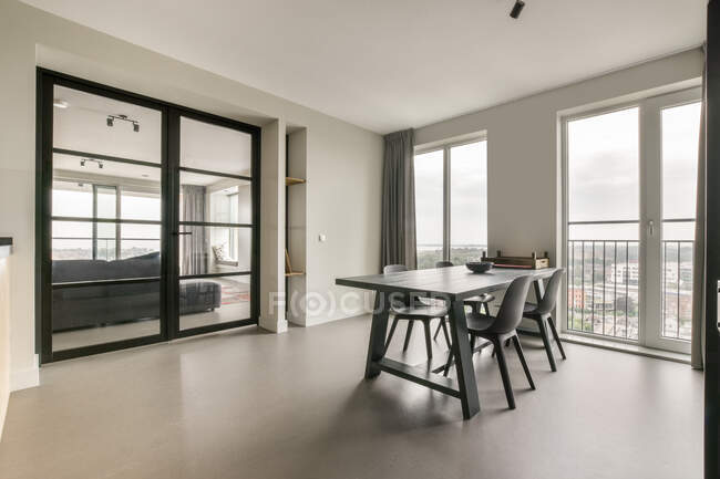 Moderne Wohnung mit geräumigem Esszimmer mit leerem Tisch und Stühlen vor großen Fenstern am Tag — Stockfoto