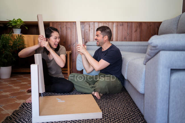 Fröhliches multirassisches Paar schaut einander beim Spielen mit Tischbeinen auf Teppich im Zimmer an — Stockfoto