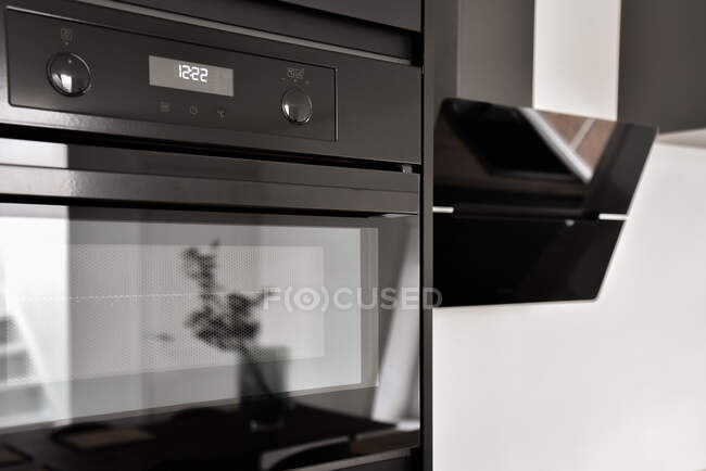 Negro moderno construido en el horno con pantalla digital de tiempo cerca de la capucha en la cocina elegante en apartamento moderno - foto de stock