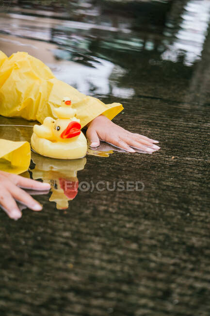 Niño de la cosecha en impermeable jugando con patos de plástico reflejándose en charco ondulado en tiempo lluvioso - foto de stock