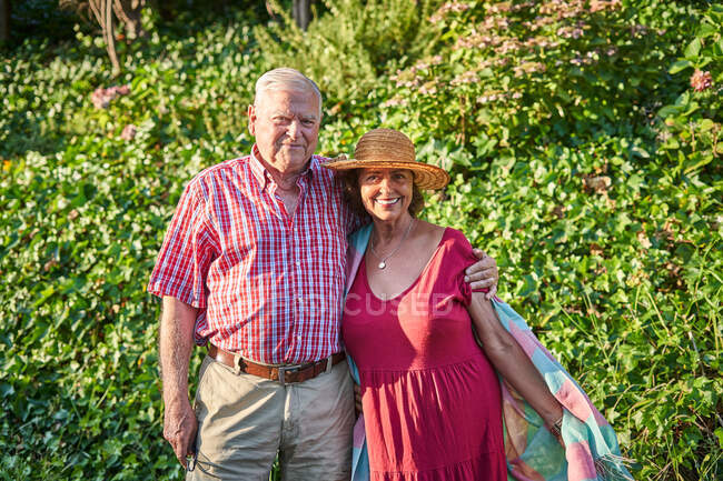 Gentile coppia anziana accarezzando guardando la fotocamera con tenerezza mentre in piedi vicino ad arbusti in natura — Foto stock